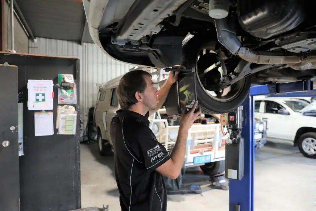 Car mechanic troubleshooting a car issue under the hood, vehicle securely lifted on a platform in a professional repair shop.