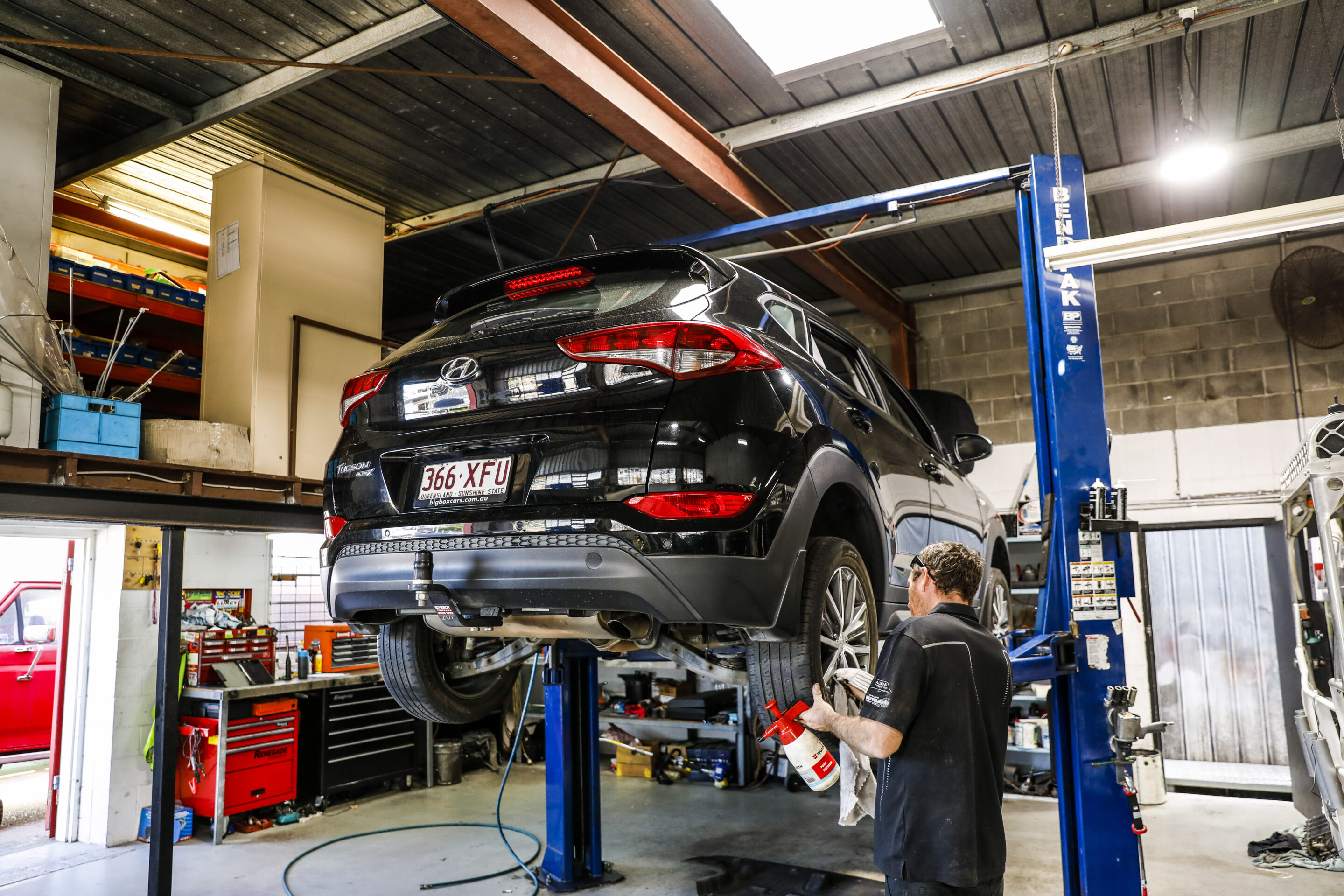 Car mechanic working on a vehicle under the hood of a car, inside a workshop or garage more alt text