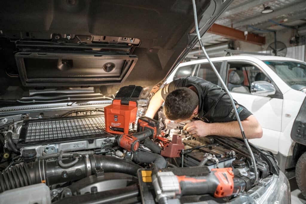 Mechanic working on a car engine under the hood in a garage