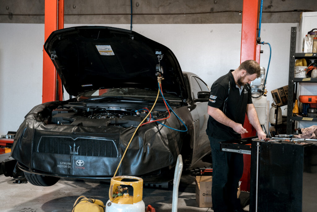 Car mechanic servicing a vehicle engine in a workshop.