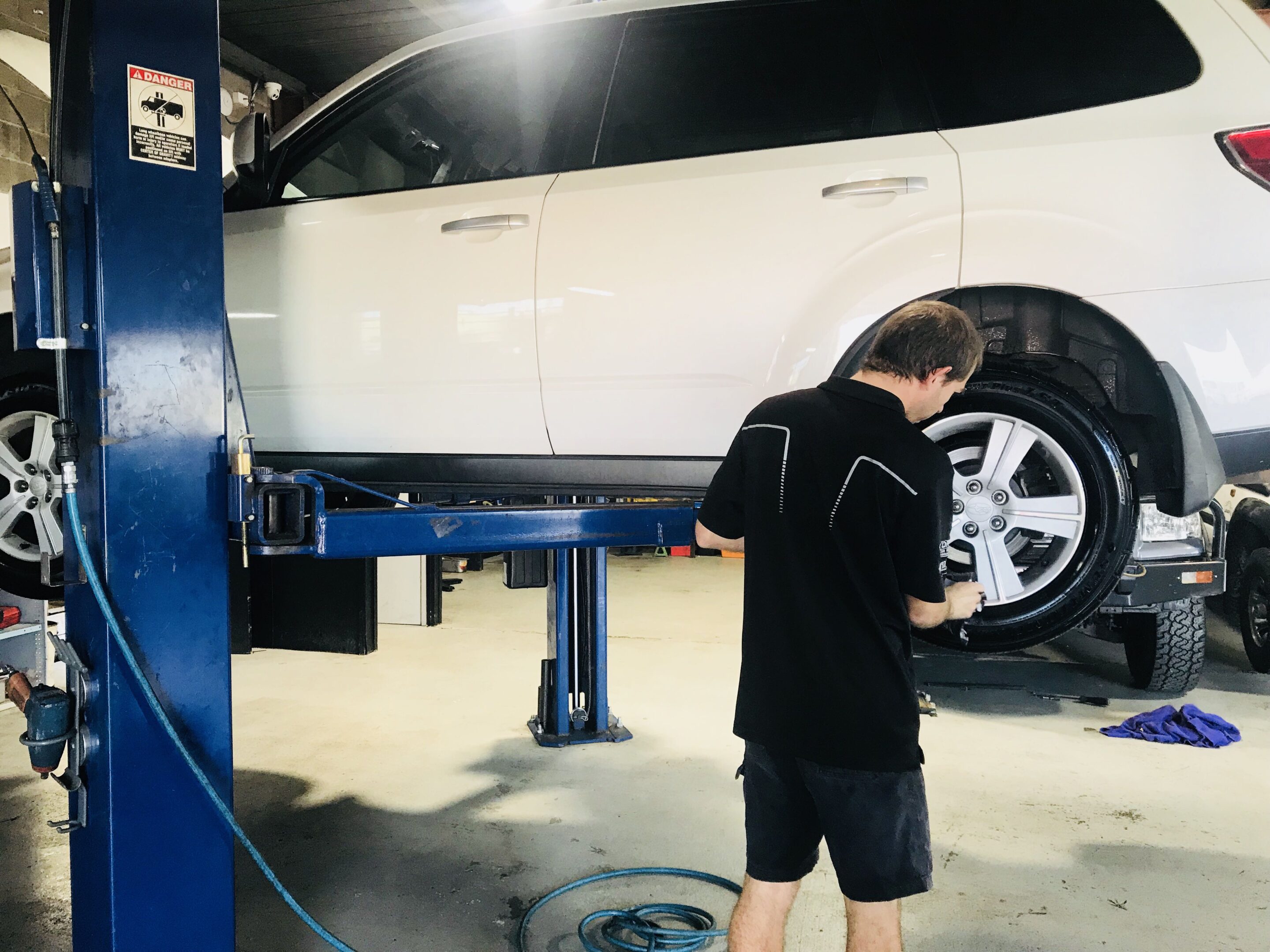 Car mechanic performing repairs on the engine of a lifted vehicle in a workshop.