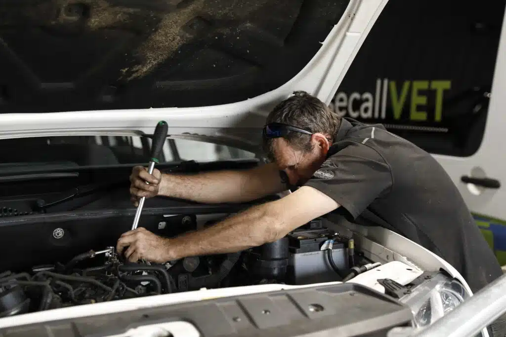Car mechanic servicing a vehicle with the engine compartment open in a workshop.