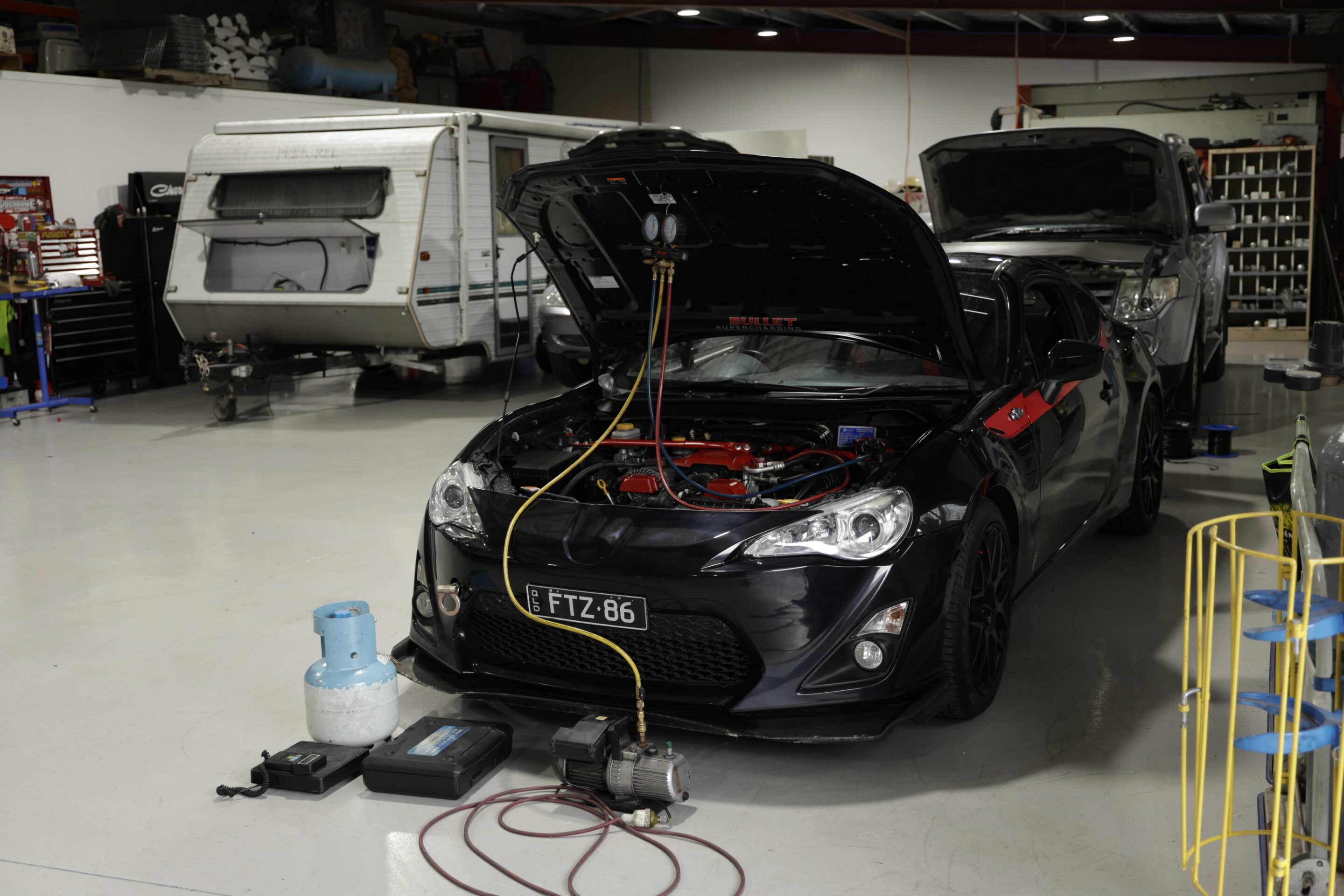 Car undergoing repairs in a workshop, with the hood open for access to the engine.