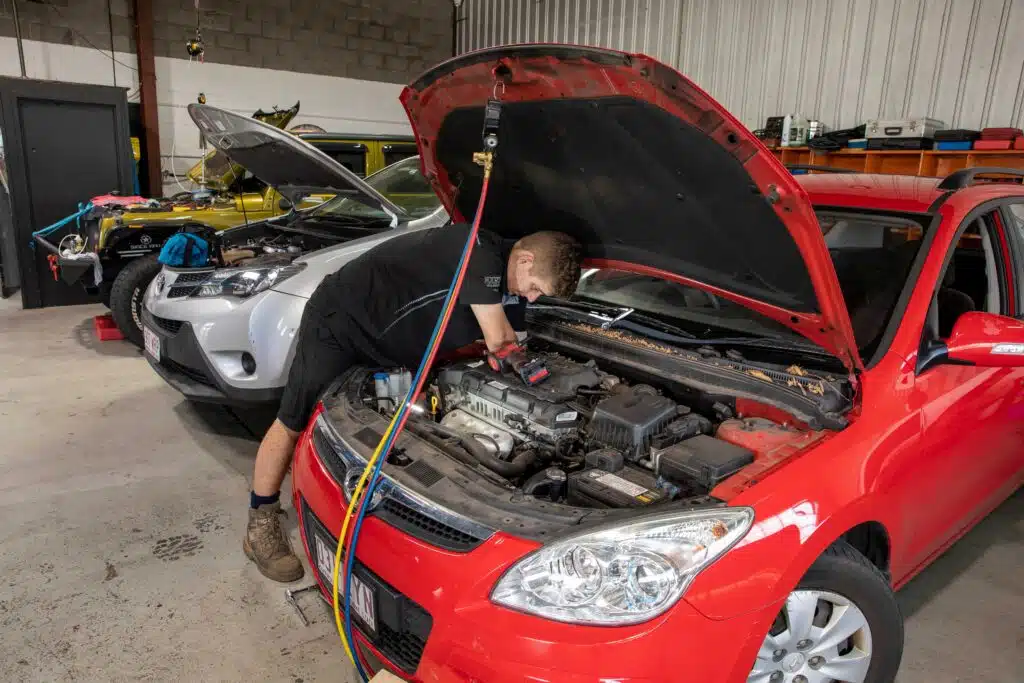 Car mechanic in a workshop diagnosing a vehicle with the engine compartment exposed