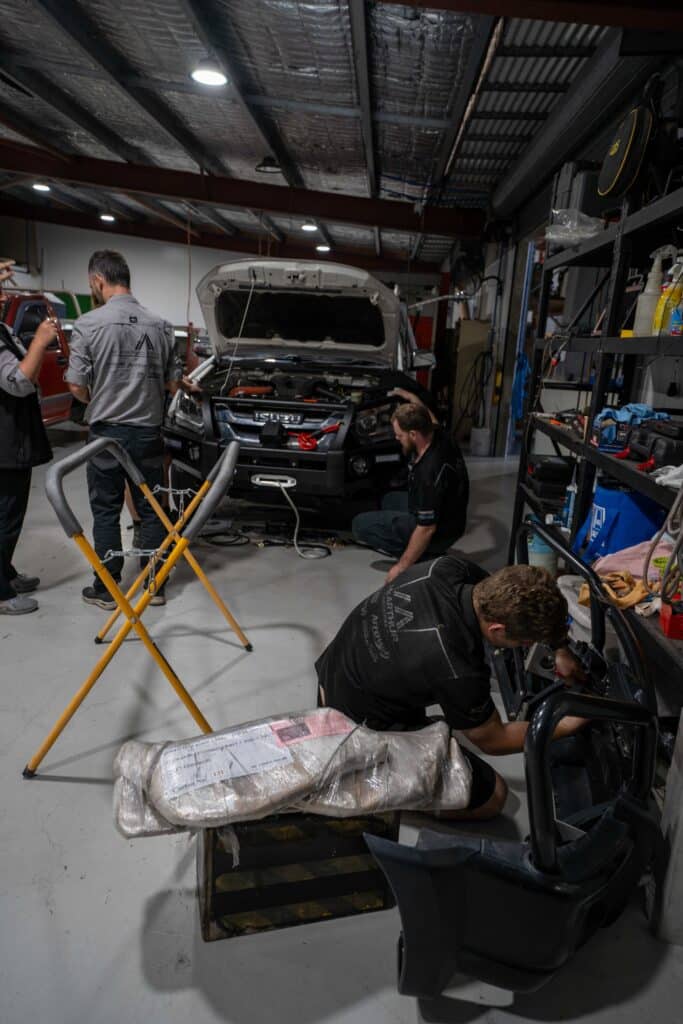 Car mechanics in a workshop using tools to diagnose or repair a vehicle with the engine compartment open