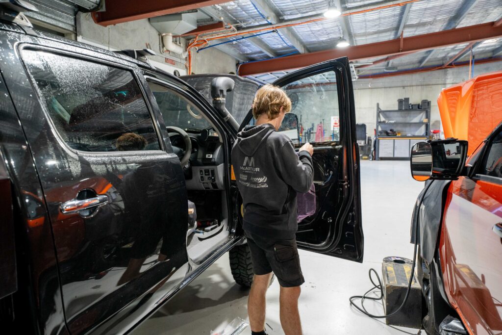 Car mechanic troubleshooting a car problem inside the vehicle with the aid of tools in a professional repair shop.