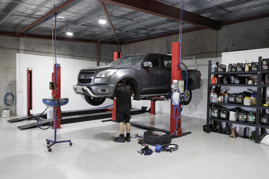 Car mechanic working on the undercarriage of a lifted vehicle in a workshop