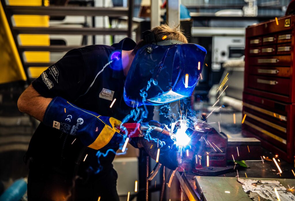 Car mechanic working on a vehicle cutting metal with sparks flying all over, inside a workshop or garage more alt text