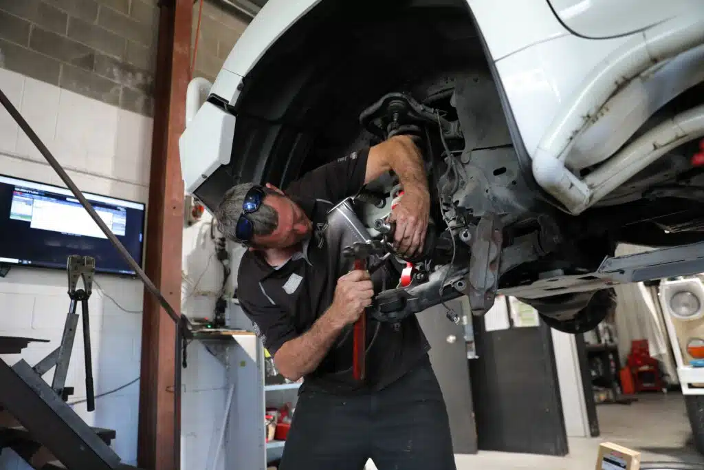 Car mechanic troubleshooting a car issue beneath the open hood in a professional repair shop.