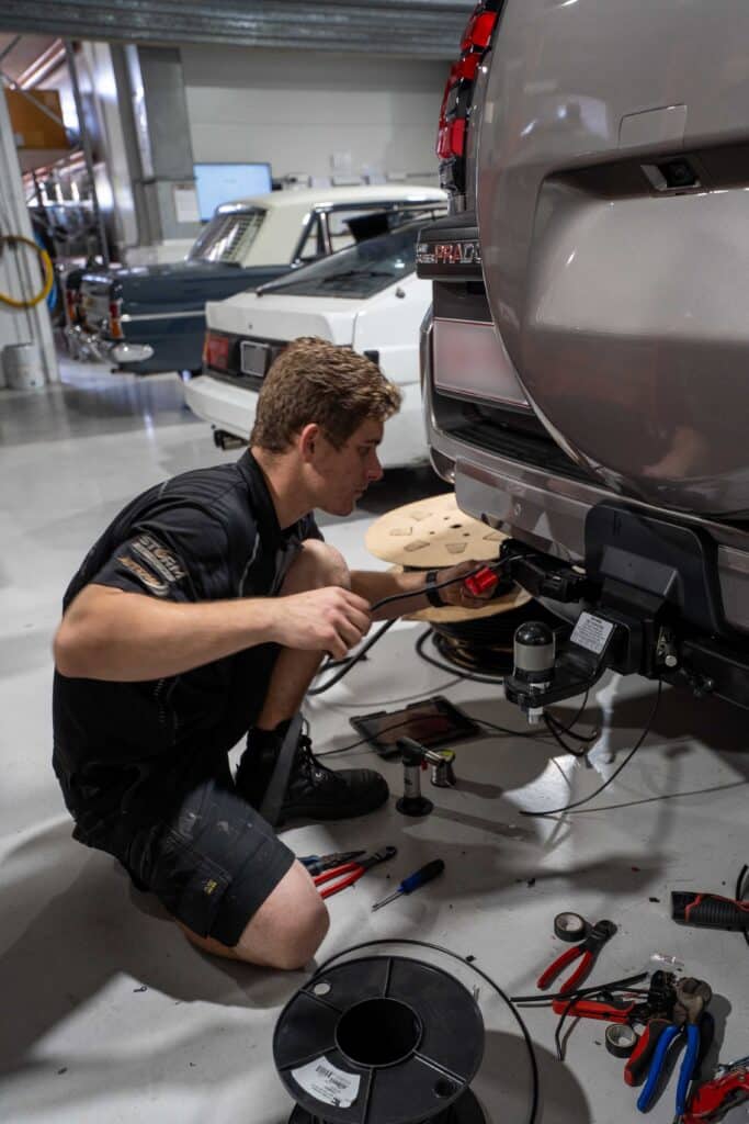 Car mechanic working on a vehicle under the hood, inside a workshop or garage more alt text